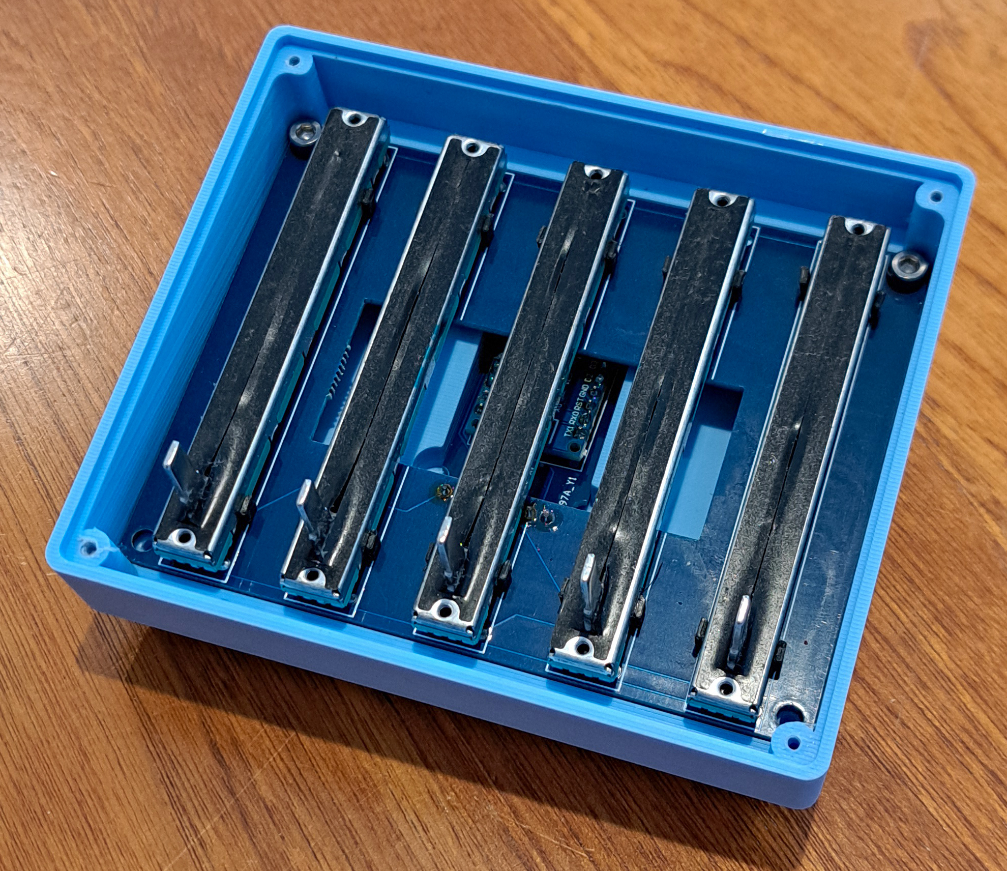 Internal view of the audio mixer showing five slider potentiometers mounted inside the blue enclosure
