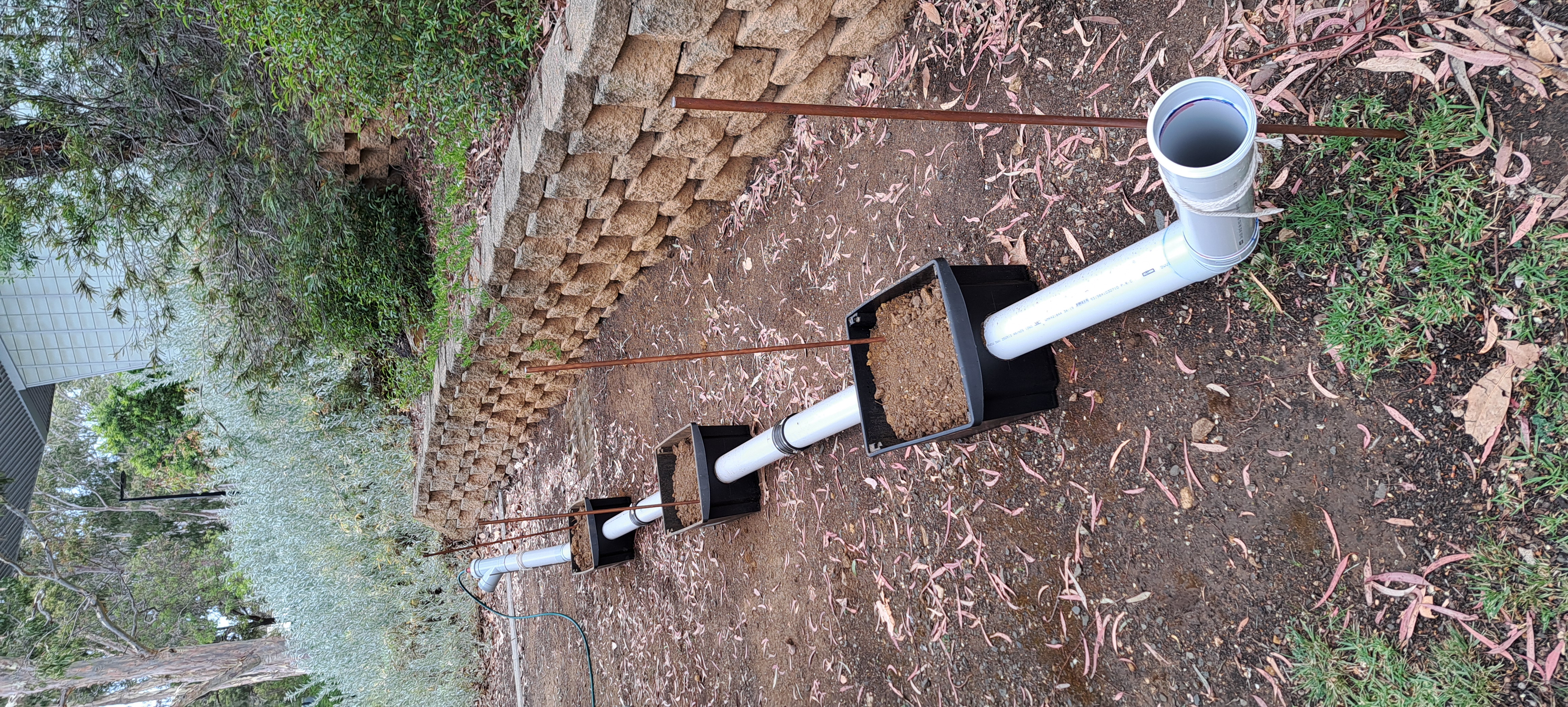 Outdoor Sewer Serpent pipe test rig with PVC pipe, soil boxes, grounding rods, and surrounding field setup